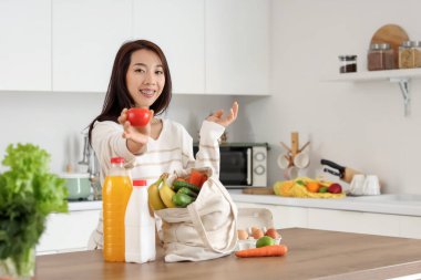 Genç Asyalı kadın mutfaktaki marketten taze ürünleri çıkarıyor.