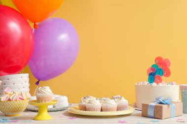 Farklı tatlılar, hediyeler ve sarı duvarlı doğum günü partisi için balonlar.