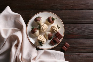 Tahta arka planda çikolata kaplı çilek tabağı.