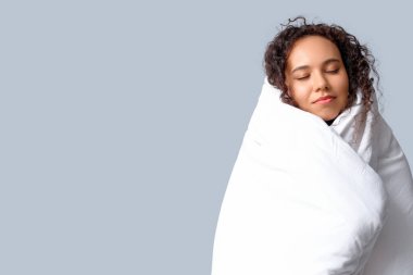 Gri arka planda battaniyesi olan güzel, mutlu, Afro-Amerikalı bir kadın.