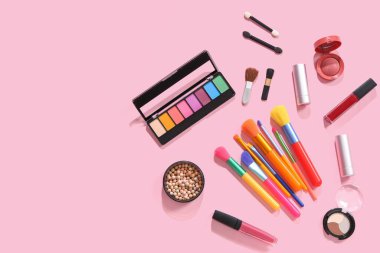Pembe arka planda kozmetik ürünlerle süslü makyaj fırçaları