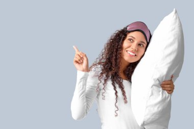 Gri arka plandaki bir şeyi gösteren yastıklı güzel, mutlu bir Afro-Amerikalı kadın.