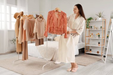 Yatak odasındaki elbise rafının yanında şık bluzu olan genç bir kadın.