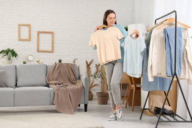 Elbise rafının yanında şık tişörtleri olan genç bir kadın.