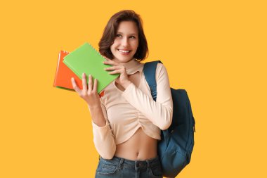 Sarı arka planda not defterleri ve sırt çantasıyla güzel bir kız öğrenci.