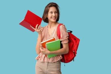 Sırt çantası ve mavi arka planda defterleri olan güzel bir kız öğrenci.