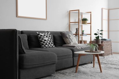 İçinde siyah kanepe, sehpa, saksı ve raf ünitesi olan güzel bir oturma odası.