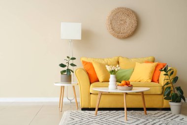 Sarı kanepeli güzel oturma odasının içi, sepetin içinde kahve masasının üzerinde meyve vazosu olan laleler.