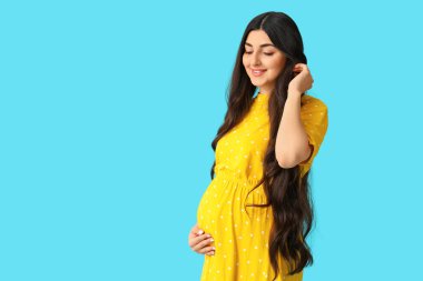 Mavi arka planda güzel, hamile bir kadın.