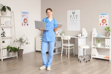 Klinikte deneme çerçevesi ve dizüstü bilgisayarı olan kadın göz doktoru.