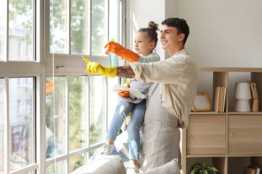 Genç baba ve kızı evde birlikte cam temizliyorlar.