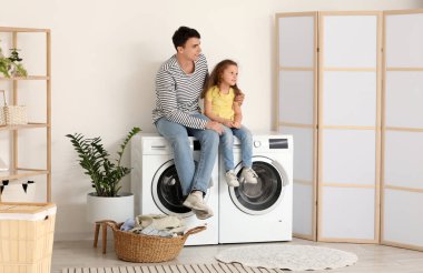 Genç baba ve kızı banyoda çamaşır makinesinde oturuyorlar.