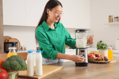 Genç Asyalı kadın mutfakta blender ile smoothie yapıyor.