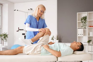 Rehabilitasyon merkezindeki kanepede yatan genç adamla çalışan kadın fizyoterapist.
