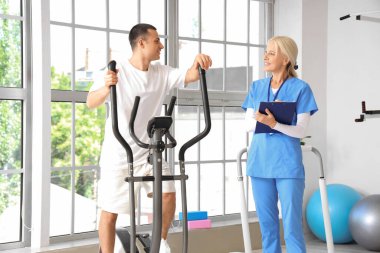 Rehabilitasyon merkezinde genç bir adamla egzersiz yapan kadın fizyoterapist.