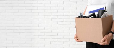 Beyaz tuğlalı arka planda kişisel eşyaları olan kovulmuş genç adam, yakın plan.