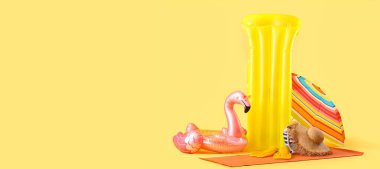 Şişme yüzük, yüzme şiltesi, sarı arka planda şemsiye ve plaj aksesuarları. Mesaj için yer var. Yaz tatili