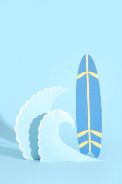 Mini sörf tahtası ve mavi zemin üzerinde kağıt dalgaları olan yaratıcı kompozisyon