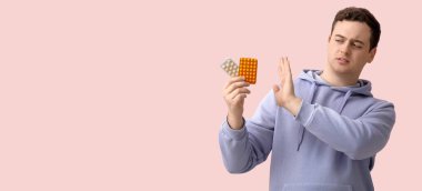 Genç adam pembe arka planda hapları reddediyor.