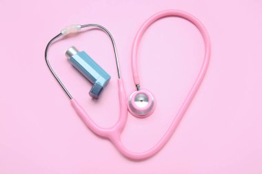 Astım spreyi ve pembe arka planda steteskop.