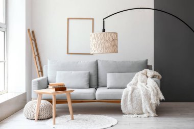 Işıl ışıl oturma odasının içi rahat gri kanepe ve taburede kitaplar.