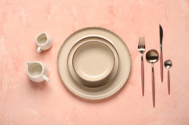 Pembe masada temiz tabak, kase ve çatal bıçak takımı var.