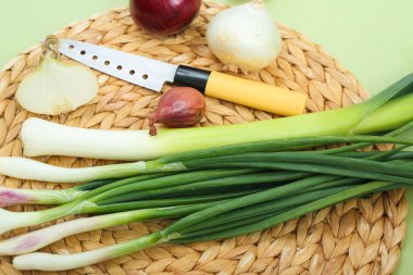 Yeşil arka planda farklı soğan türleri olan hasır paspas, yakın plan.