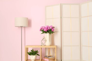 Raflarda pembe şakayık vazosu, giyinme masası ve renkli duvarın yanında yer lambası.