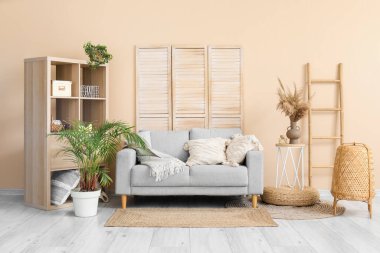 Aydınlık oturma odasının içinde şık gri kanepe, raf ünitesi, katlanır ekran ve merdiven