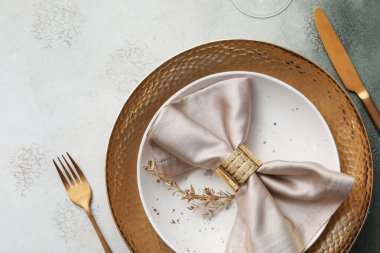 Gri masa üzerinde altın yapraklar ve çatal bıçak takımı olan zarif bir masa.