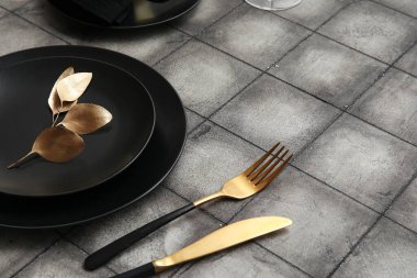 Siyah tabaklar, altın yapraklar ve gri fayanslı çatal bıçaklar.