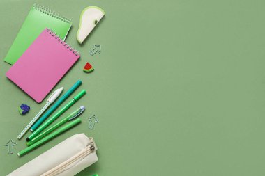 Farklı okul kağıtları ve yeşil arkaplan üzerine not defterleri olan bej renkli kalem çantası.