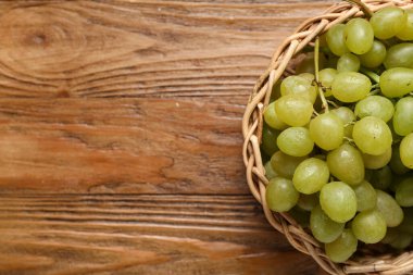 Tahta arka planda tatlı yeşil üzümlü hasır kase.