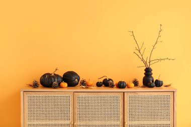 Ahşap dolap, sarı duvarın yanında balkabakları ve konileri var.