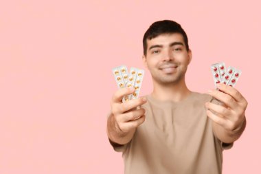 Pembe arka planda A vitamini hapları olan genç adam, yakın plan.