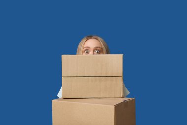 Mavi arka planda karton kutuları olan genç bir kadın.