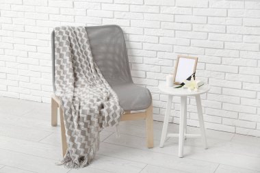 Boş cenaze çerçeveli masa, yanan mum ve ışıklı tuğla duvarın yanındaki sandalye.