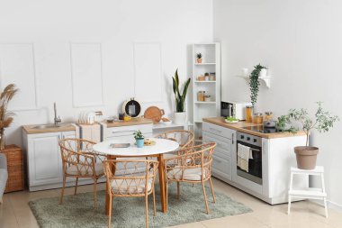 Yeşil bitkilerle, tezgahlarla ve yemek masalarıyla aydınlık mutfağın içinde.