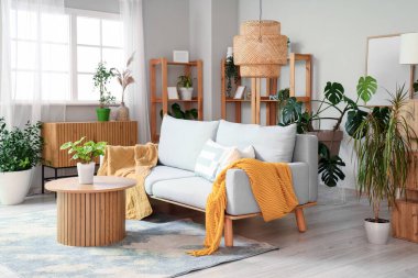 Oturma odasının içinde yeşil bitkiler, kanepe ve masa var.