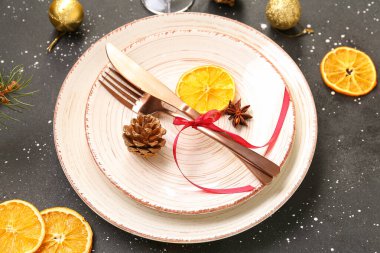 Kurumuş portakal dilimleri, toplar ve siyah arka planda çam kozalağı ile Noel sofrası.