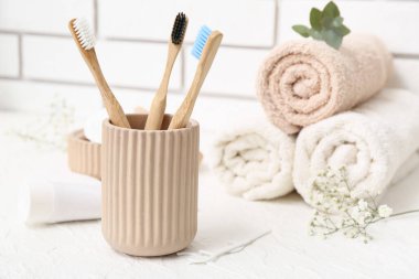 Elinde diş fırçası ve banyo malzemeleri olan tutucu hafif tuğla duvarın yanındaki masada.