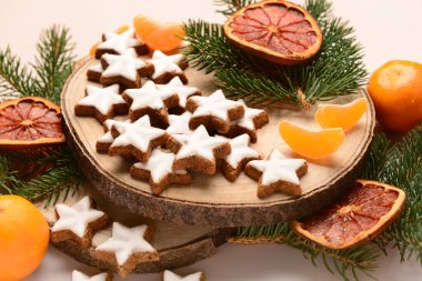 Mandarin, kurutulmuş portakal ve köknar dallarıyla bej arka planda yıldız şeklinde zencefilli kurabiye tahtası.