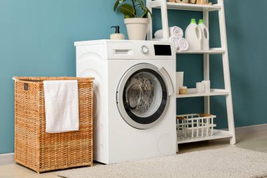 Çamaşır sepeti, çamaşır makinesi ve raf ünitesi olan odanın içi.
