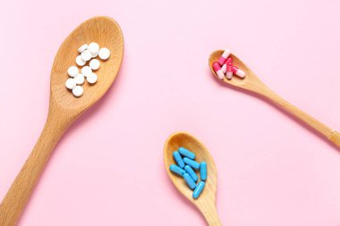 Ahşap kaşıklar ve pembe arka planda farklı haplar.