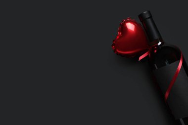 Siyah arka planda kalp şeklinde hava balonu olan bir şişe şarap. Sevgililer Günü kutlaması