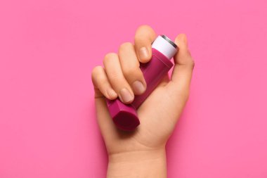 Pembe arka planda astım spreyi olan bir çocuk eli.