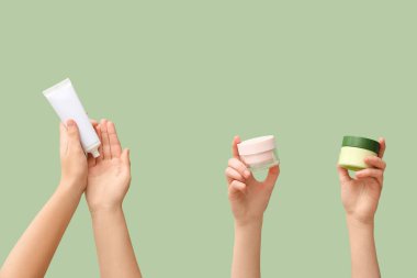 Yeşil arka planda farklı kozmetik kremi olan kadın elleri