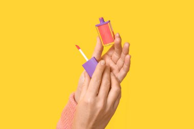 Sarı arka planda sıvı ruj tutan eller