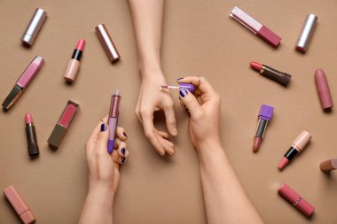 Kahverengi arka planda farklı ruj izleri olan kadın elleri.