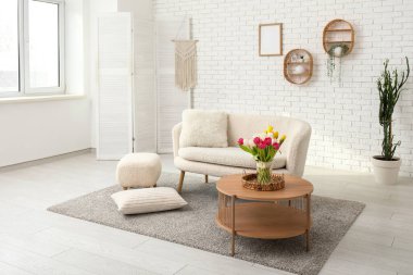 Beyaz çatı katı tarzı oturma odasının içinde kanepe, çiçekler ve kahve masası var.